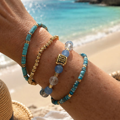 Armbandenset Blue Coast met blauwe kralen en goudkleurige details gedragen op het strand