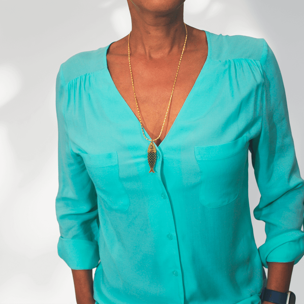 Model draagt de lange goudvergulde damesketting Fish van SummerGear met blauwgroene vishanger bij een turquoise blouse